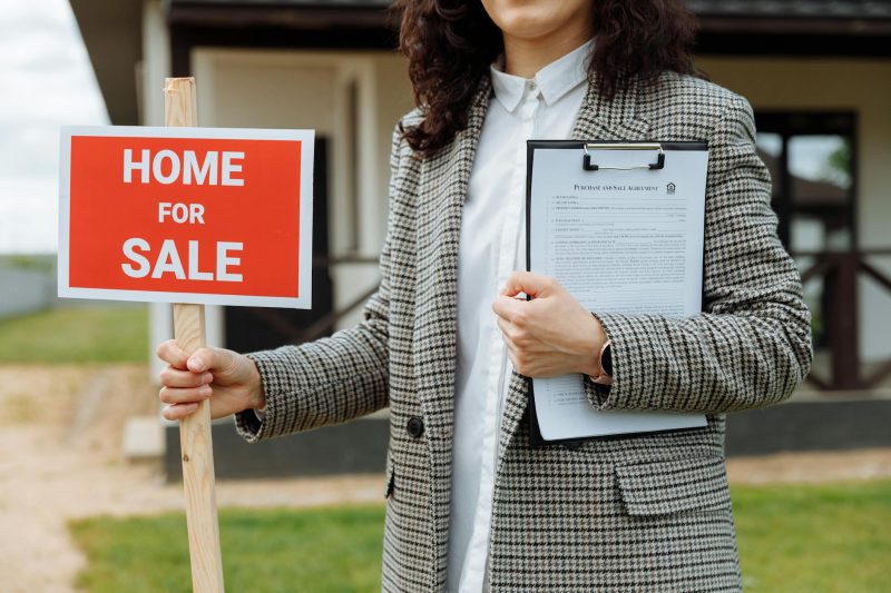 Home 2 A real estate agent holding a home for sale sign and clipboa 1779814844